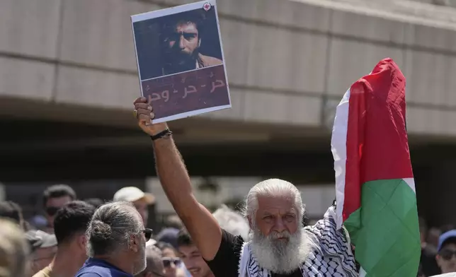 A supporter of Lebanese pro-Palestinian militant George Abdallah, who was serving a life sentence for complicity in the 1982 murders of an American and an Israeli diplomat in Paris, holds up a poster with his portrait and a Palestinian flag as he waits for Abdallah's arrival at Rafic Hariri International Airport in Beirut, Lebanon, Friday, July 25, 2025. The Arabic reads: "Free, free, and free" (AP Photo/Hussein Malla)