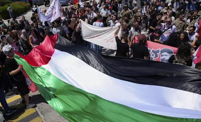 Supporters of Lebanese pro-Palestinian militant George Abdallah, who was serving a life sentence for complicity in the 1982 murders of an American and an Israeli diplomat in Paris, hold a large Palestinian flag and banners as they gather outside Rafic Hariri International Airport to welcome his return, in Beirut, Lebanon, Friday, July 25, 2025. (AP Photo/Hussein Malla)