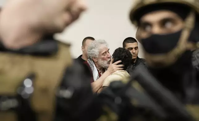Lebanese pro-Palestinian militant Georges Abdallah, center left, who was serving a life sentence for complicity in the 1982 murders of a U.S. and an Israeli diplomat in Paris, is greeted by a supporter and surrounded by security forces upon his arrival in Qobayat village, in northern Akkar province, Lebanon, Friday, July 25, 2025. (AP Photo/Hassan Ammar)