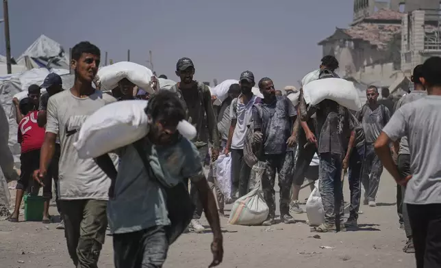 Palestinians carry sacks of flour unloaded from a humanitarian aid convoy that reached Gaza City from the northern Gaza Strip, Sunday, July 27, 2025. (AP Photo/Abdel Kareem Hana)