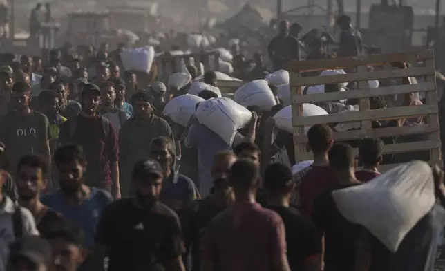 Palestinians carry sacks of flour unloaded from a humanitarian aid convoy that reached Gaza City from the northern Gaza Strip, Saturday, July 26, 2025. (AP Photo/Jehad Alshrafi)