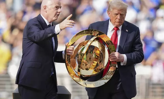FIFA President Gianni Infantino, left, and President Donald Trump carry the championship trophy after the Club World Cup final soccer match between Paris Saint-Germain and Chelsea in East Rutherford, N.J., Sunday, July 13, 2025. (AP Photo/Frank Franklin II)