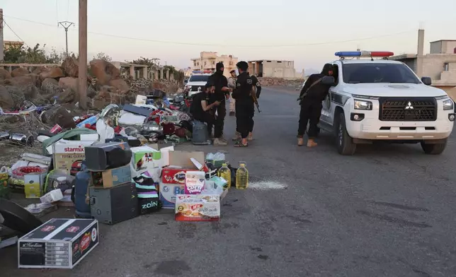 Government soldiers stand next to confiscate items stolen during clashes in Sweida city between government forces and Druze militias at a checkpoint in Mazraa village, southern Syria, Tuesday, July 15, 2025. (AP Photo/Omar Albam)
