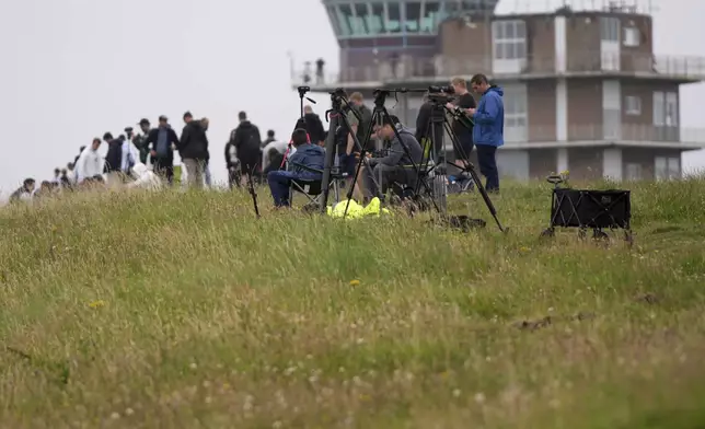 Visitors and plane spotters stand on a hill overviewing Prestwick Airport in Ayrshire, Scotland, Friday, July 25, 2025 ahead of the arrival of President Donald Trump.(AP Photo/Alastair Grant)