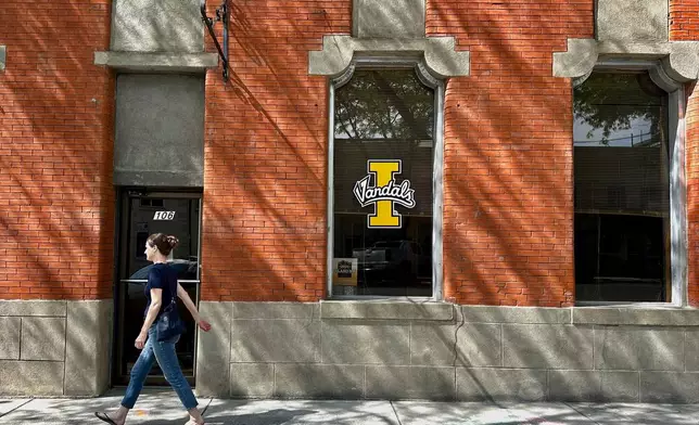 A person walks on a downtown street in Moscow, Idaho, in front of a building with a University of Idaho logo on a window on Tuesday, July 1, 2025. (AP Photos/Manuel Valdes)