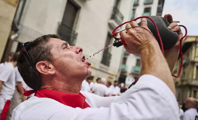 A reveler drinks wine as he takes part in the official start of nine days of uninterrupted partying in Pamplona's famed running-of-the-bulls festival in Pamplona, Spain, Sunday, July 6, 2025. (AP Photo/Miguel Oses)