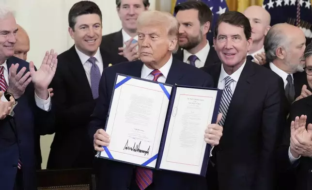President Donald Trump holds up the GENIUS Act, a bill that regulates stablecoins, a type of cryptocurrency, after he signs the bill in the East Room of the White House, Friday, July 18, 2025, in Washington. (AP Photo/Alex Brandon)