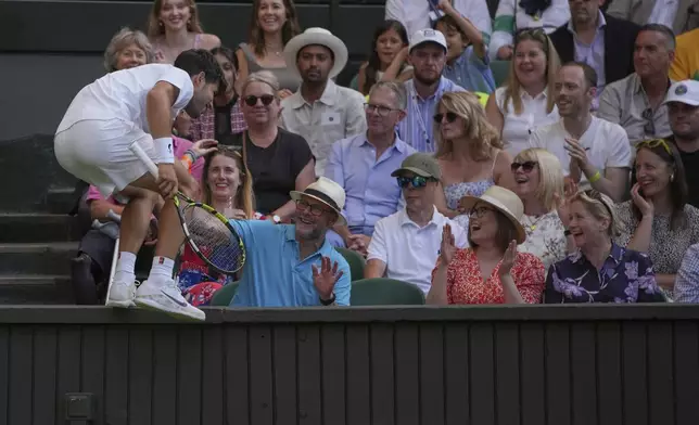 Carlos Alcaraz of Spain jumps onto a ledge near the crowd as he tries to chase down a shot from Jan-Lennard Struff of Germany speeds past during a third round men's singles match at the Wimbledon Tennis Championships in London, Friday, July 4, 2025. (AP Photo/Kin Cheung)
