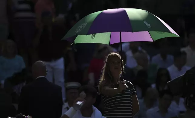A ballgirl shield Carlos Alcaraz of Spain from the sun during a change of ends break against Jan-Lennard Struff of Germany during a third round men's singles match at the Wimbledon Tennis Championships in London, Friday, July 4, 2025. (AP Photo/Kin Cheung)
