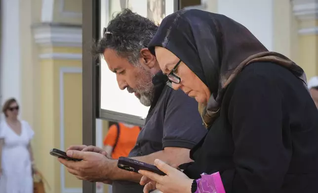 Pedestrians pause to look at their phones in St. Petersburg, Russia, on Monday, July 14, 2025. (AP Photo/Dmitri Lovetsky)