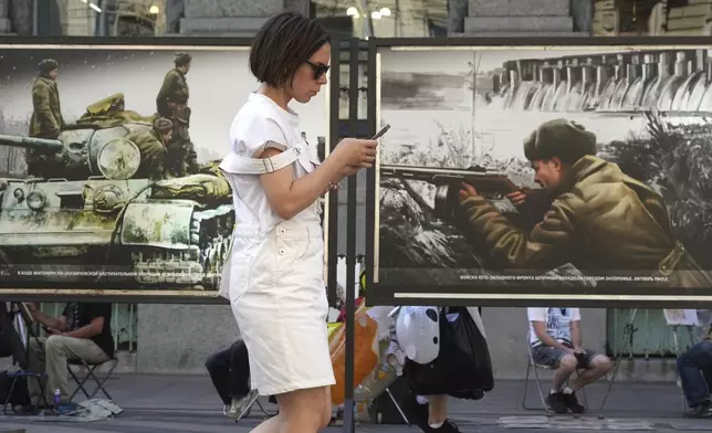 A woman looks at her phone while passing a street exhibition of World War II-era colorized photos in St. Petersburg, Russia, on Monday, July 14, 2025. (AP Photo/Dmitri Lovetsky)