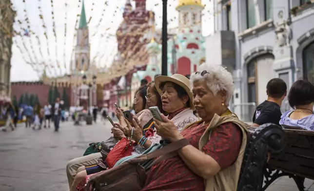 Tourists sitting near the Kremlin in Moscow look at their phones on Wednesday, July 16, 2025. (AP Photo/Alexander Zemlianichenko)