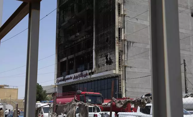 Firefighters gather in front of a burnt building in Kut, Iraq, Thursday, July 17, 2025 following a fire. (AP Photo/ Hadi Mizban)