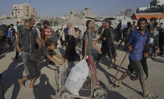 Palestinians carry sacks of flour unloaded from a humanitarian aid convoy that reached Gaza City from the northern Gaza Strip, Saturday, July 26, 2025. (AP Photo/Jehad Alshrafi)