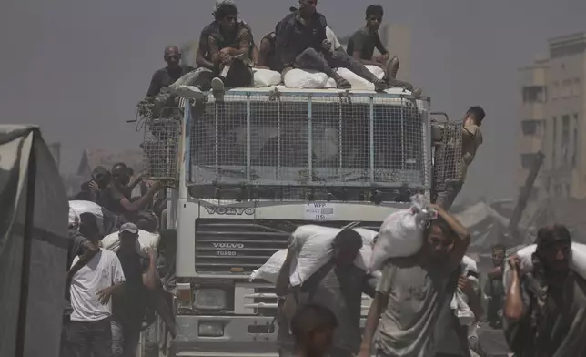 Palestinians carry sacks of flour unloaded from a humanitarian aid convoy that reached Gaza City from the northern Gaza Strip, Sunday, July 27, 2025. (AP Photo/Jehad Alshrafi)