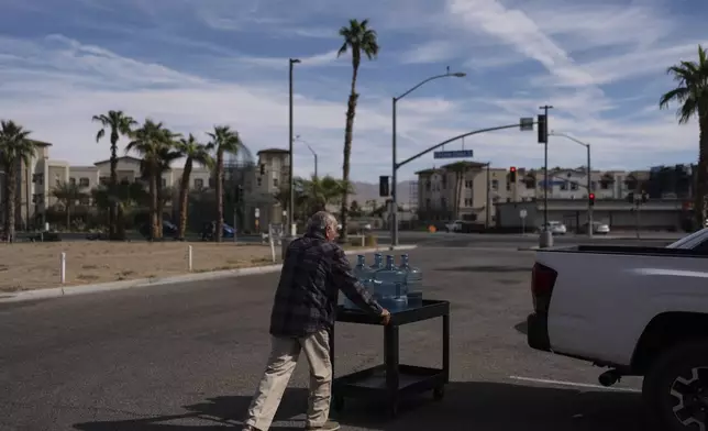 Agustin Toledo, a mobile home resident in Southern California's eastern Coachella Valley, pushes a cart carrying refilled water jugs to his pickup truck in Coachella, Calif., Wednesday, Oct. 30, 2024. (AP Photo/Jae C. Hong)