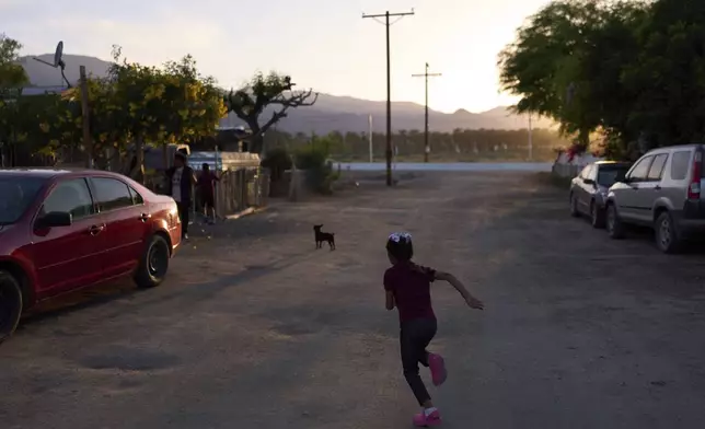 A girl runs across a dirt road in a mobile home park as the sun sets in Oasis, Calif., Monday, April 14, 2025. (AP Photo/Jae C. Hong)