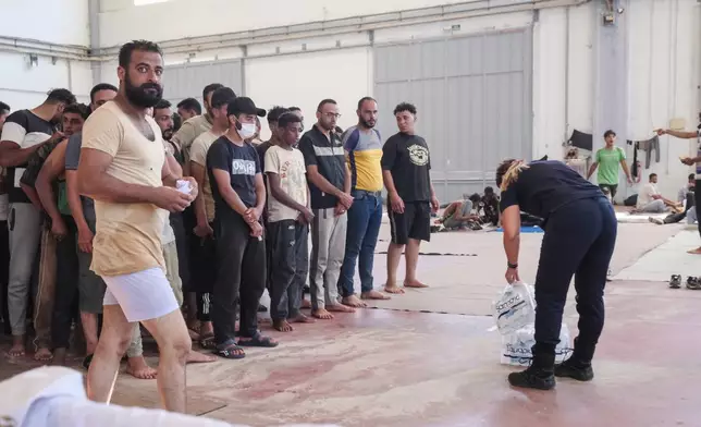 A Greek coast guard gives water to migrants from Africa as they take a shelter in Agia port, Chania, Crete island, Greece, Monday, July 7, 2025. (AP Photo/Giannis Angelakis)