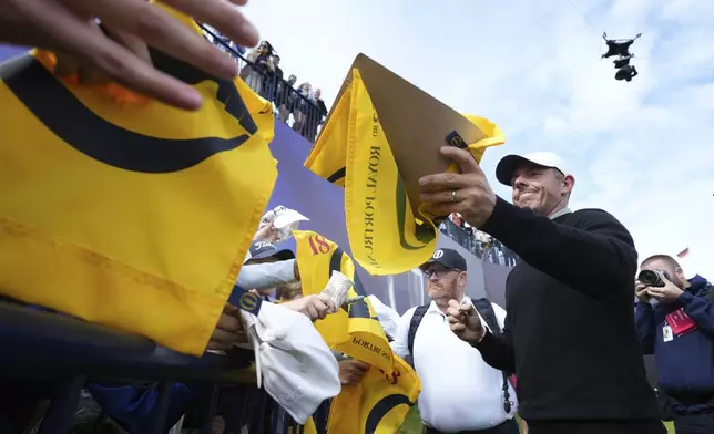 Rory McIlroy of Northern Ireland signs autographs on the 18th green watched by the new Spidercam, top right, following a practice round for the British Open golf championship at the Royal Portrush Golf Club, Northern Ireland, Tuesday, July 15, 2025. (AP Photo/Jon Super)