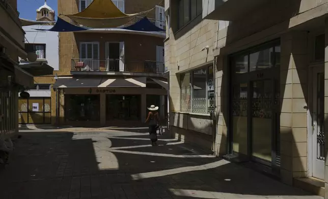 A woman walks at a pedestrian road during a hot day in the capital Nicosia, Cyprus, Wednesday, July 9, 2025. (AP Photo/Petros Karadjias)