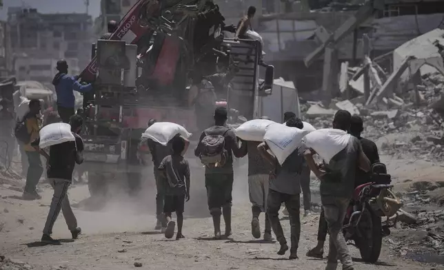 Palestinians carry sacks of flour unloaded from a humanitarian aid convoy that reached Gaza City from the northern Gaza Strip, Tuesday, July 22, 2025. (AP Photo/Jehad Alshrafi)
