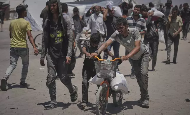 Palestinians carry sacks of flour unloaded from a humanitarian aid convoy that reached Gaza City from the northern Gaza Strip, Tuesday, July 22, 2025. (AP Photo/Jehad Alshrafi)