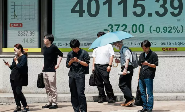 People stand in front of an electronic stock board showing Japan's Nikkei index at a securities firm Tuesday, July 1, 2025, in Tokyo. (AP Photo/Eugene Hoshiko)