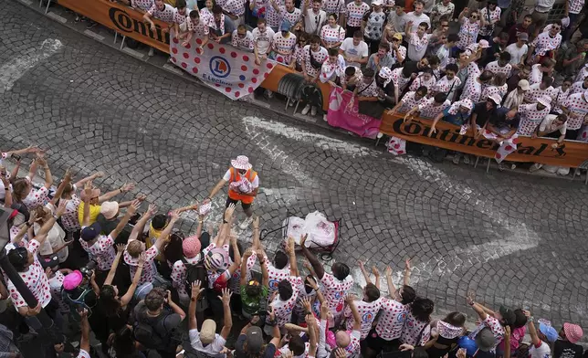 A man distributes publicity items to cycling fans in a packed street of the Montmartre district during the last stage of the Tour de France cycling race between Mantes-la-Ville and Paris, Sunday, July 27, 2025 in Paris (AP Photo/Laurent Cipriani)