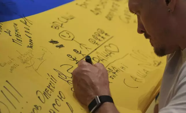 Ukraine's boxer Oleksandr Usyk signs autograph as he meets the Ukrainian war veterans, who are employees of Ukrainian power company DTEK at a hotel in Battersea Park in London, Thursday, July 17, 2025 ahead of the undisputed heavyweight champion boxing fight between Britain's Daniel Dubois and Oleksandr Usyk on Saturday. (AP Photo/Kin Cheung)