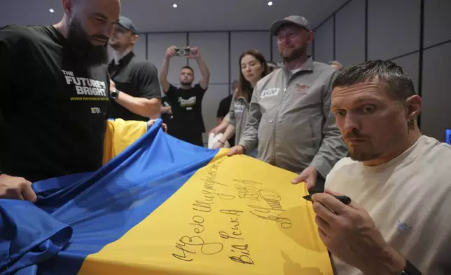Ukraine's boxer Oleksandr Usyk signs autograph as he meets the Ukrainian war veterans, who are employees of Ukrainian power company DTEK at a hotel in Battersea Park in London, Thursday, July 17, 2025 ahead of the undisputed heavyweight champion boxing fight between Britain's Daniel Dubois and Oleksandr Usyk on Saturday. (AP Photo/Kin Cheung)