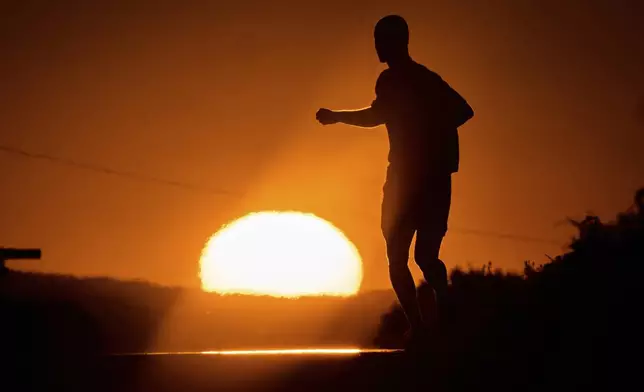 A man runs towards the rising sun on a small road on the outskirts of Frankfurt, Germany, Tuesday, July 1, 2025. (AP Photo/Michael Probst)