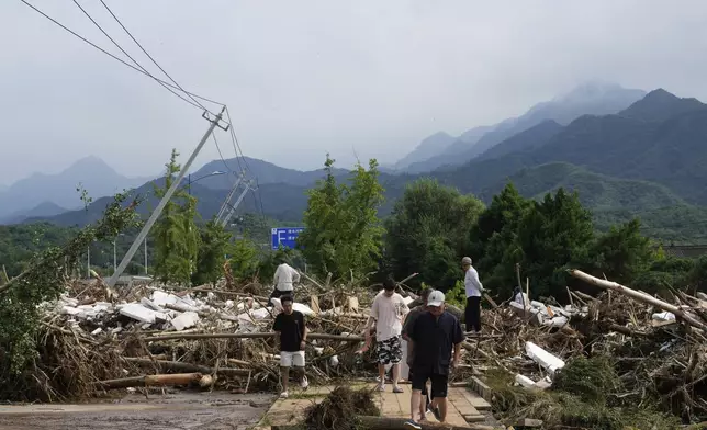 Local residents walks in front of a damaged road littered with broken tree branches after a heavy rains in Taishitun Town, Miyun district on the outskirts of Beijing, China, Monday, July 28, 2025. (AP Photo/Mahesh Kumar A.)