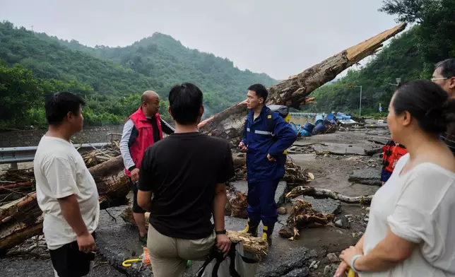 In this photo released by Xinhua News Agency, rescuers talk to villagers on a road damaged by floodwaters in Miyun District as continuous rain fall triggers alerts, in north of Beijing on July 27, 2025. (Ju Huanzong/Xinhua via AP)