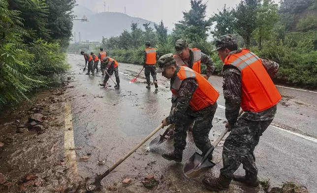 In this photo released by Xinhua News Agency, members of the Chinese People's Armed Police Force clean up silt on a road in Miyun District as continuous rain fall triggers alerts, in north of Beijing on July 27, 2025. (Wang Xiqing/Xinhua via AP)