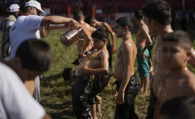 A young wrestler is doused in oil during the 664th annual Historic Kirkpinar Oil Wrestling championship, in Edirne, northwestern Turkey, Sunday, July 6, 2025.(AP Photo/Khalil Hamra)