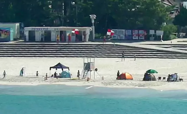 In this image taken from a fixed position video, peopel wave tsunami warning flags, seen at the background, to beachgoers immidiately after a strong earthquake near Russia’s Kamchatka Peninsula, in Shirahama, Wakayama prefecture, western Japan Wednesday, July 30, 2025. (Kyodo News via AP)