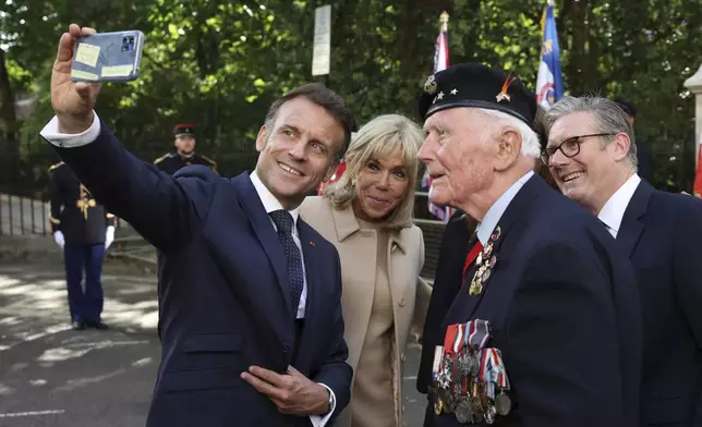 French President Emmanuel Macron takes a selfie with his wife Brigitte Macron, Britain's Prime Minister Keir Starmer and Veteran Eugenius Nead, as they attend a ceremony at the statue of former French President Charles de Gaulle, in London, Tuesday July 8, 2025. (Suzanne Plunkett/Pool Photo via AP)