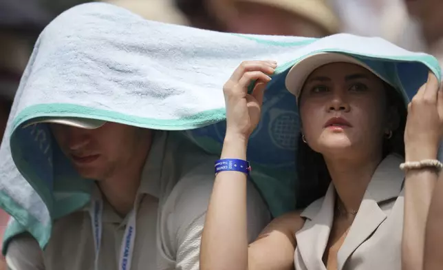 Spectators shelter from the sun as they watch Barbora Krejcikova of Czech Republic and Alexandra Eala of the Philippines during their first round women's singles match at the Wimbledon Tennis Championships in London, Tuesday, July 1, 2025. (AP Photo/Kin Cheung)