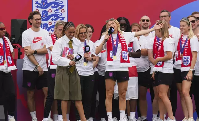 England's soccer player Chloe Kelly gestures while addressing fans next to sports presenter and former soccer player Alex Scott, left, during a homecoming victory parade and celebration outside Buckingham Palace in London, after winning the Women's Euro 2025,Tuesday, July 29, 2025.(AP Photo/Kirsty Wigglesworth)