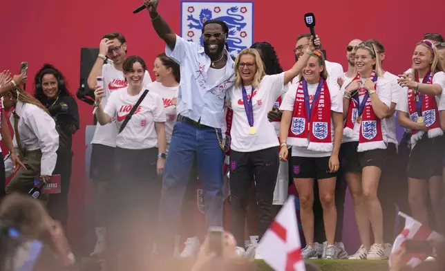 England's soccer head coach Sarina Wiegman, center right, and singer Burna Boy celebrate with players and fans during a ceremony on a stage in front of Buckingham Palace in central London, Tuesday, July 29, 2025 after their victory in the Women's EURO 2025 final.(AP Photo/Kin Cheung)