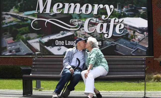 Mario and Gail Cirasunda, of Orchard Park, N.Y., share a kiss on a bench following a Memory Cafe event at the National Comedy Center Monday, May 5, 2025, in Jamestown, N.Y. (AP Photo/Jeffrey T. Barnes)