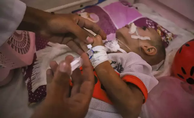 A doctor administers medication to 3-year-old Amr al-Hams, who lies in a hospital bed with brain damage caused by an Israeli strike on his family's tent in April, at Nasser Hospital in Khan Younis, Gaza Strip, Wednesday, June 25, 2025. (AP Photo/Mariam Dagga)