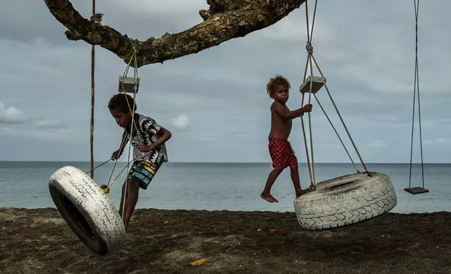 Children play on an uprooted tree along a beach in Mele, Vanuatu that was once lined with vegetation, now largely lost to storms, erosion and other environmental pressures on Saturday, July 19, 2025. (AP Photo/Annika Hammerschlag)