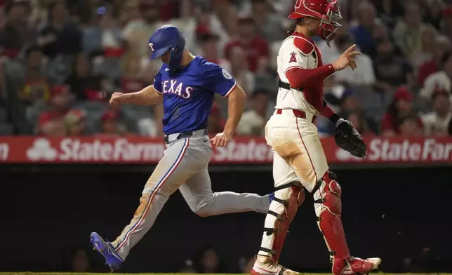 Texas Rangers' Wyatt Langford, left, scores on a single by Evan Carter as Los Angeles Angels catcher Logan O'Hoppe stands by during the eighth inning of a baseball game Wednesday, July 30, 2025, in Anaheim, Calif. (AP Photo/Mark J. Terrill)