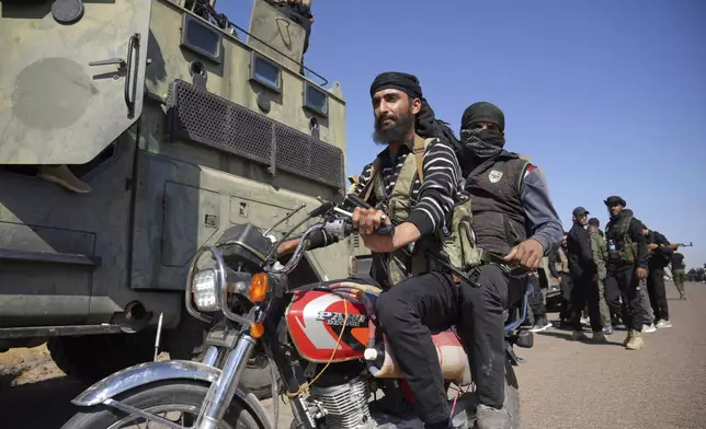Two fighters from the Sunni Bedouin clans, ride their motorcycle as they pass by Syrian government security forces deployed on the outskirts of the Sweida province where clashes erupted between Druze militias and Sunni Bedouin clans, southern Syria, Monday, July 14, 2025. (AP Photo/Malek Khattab)