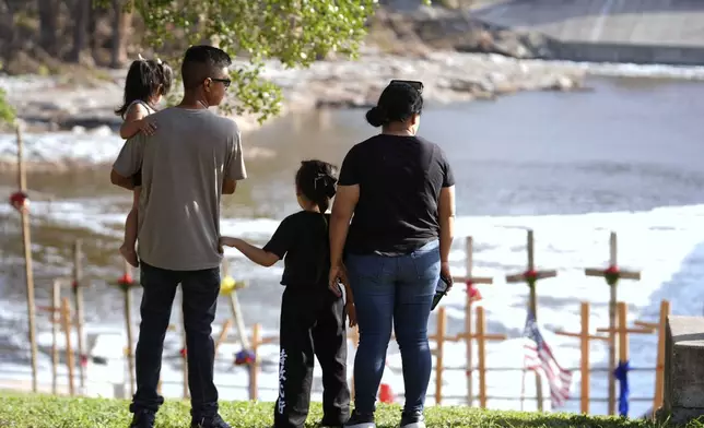 Kerrville residents Edgar Rojas, second from left, and his wife Perla, alongside daughters Emily, left, and Olivia, visit a memorial for flood victims along the Guadalupe River on Thursday, July 10, 2025, in Kerrville, Texas. (AP Photo/Gerald Herbert)