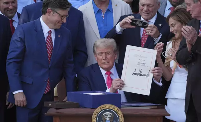 President Donald Trump holds his signed signature bill of tax breaks and spending cuts at the White House, Friday, July 4, 2025, in Washington, as House Speaker Mike Johnson of La., left, watches and Rep. Steve Scalise, R-La., takes a photo. (AP Photo/Evan Vucci)