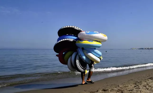 A buoys vendor walks on the beach in Algiers, Friday, July 18, 2025. (AP Photo/Fateh Guidoum)