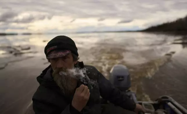 Jake Pogrebinsky smokes a cigarette while diving his boat on the Yukon River looking for logs to collect, Tuesday, May 20, 2025, in Galena, Alaska. (AP Photo/John Locher)