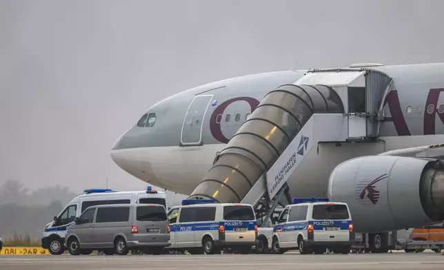 People board a Qatar Airways plane, with federal police vehicles in front of it, on the apron at Leipzig/Halle Airport, Friday, July 18, 2025, Saxony, Schkeuditz. (Jan Woitas/dpa/dpa via AP)